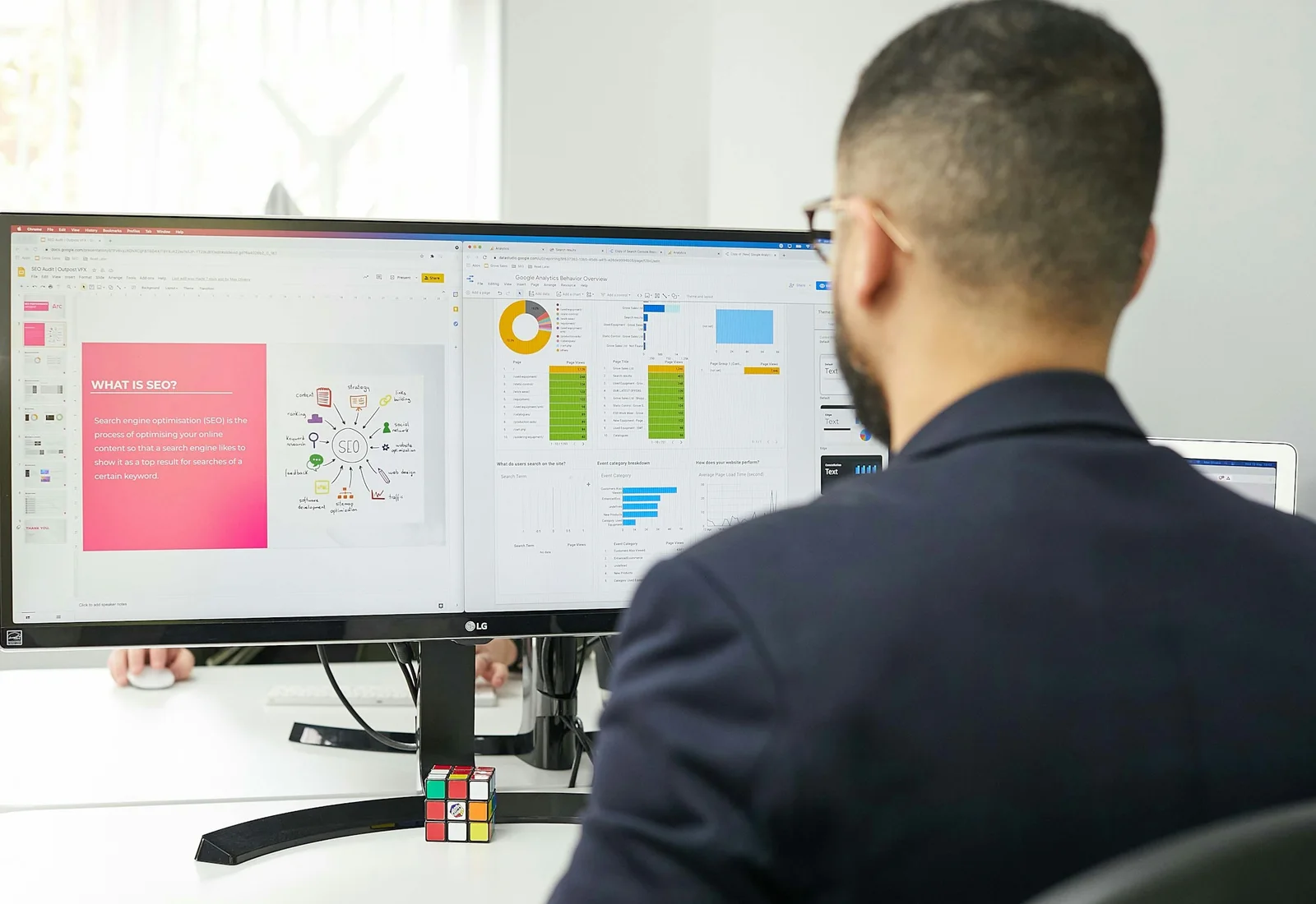 A marketing specialist reviewing an SEO presentation and website analytics on a widescreen monitor